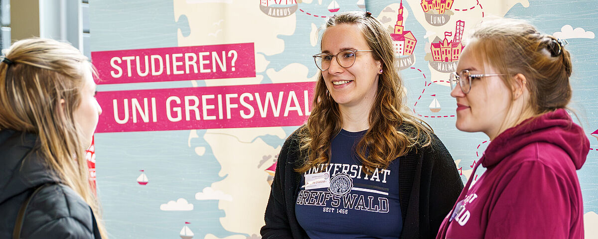 Eine interessierte Personen lässt sich an einem Stand während der Hochschulinformationstage von zwei Studentinnen beraten. 