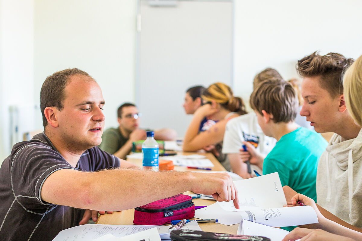 Ein Lehrer erklärt einem Schüler in einer Klasse eine Aufgabe.