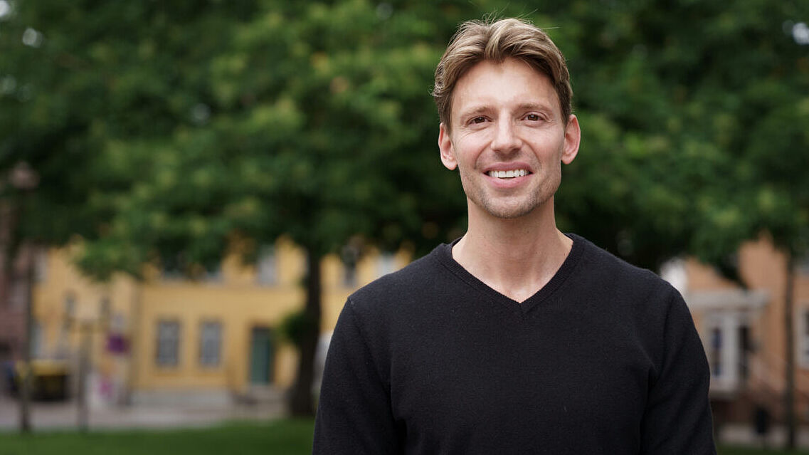 Das Foto zeigt ein Portraitbild von Prof. Dr. Nikolas Koch, im Hintergrund sind Häuser und Bäume zu erkennen.<