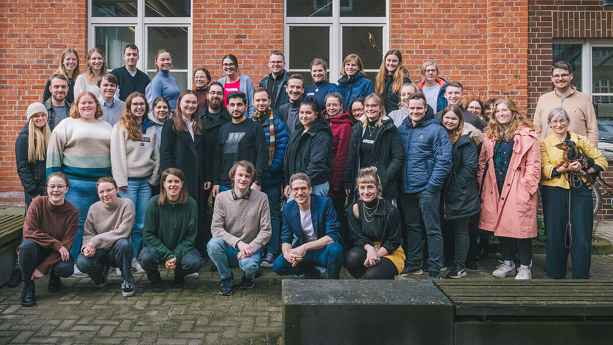 Die Teilnehmenden und ein Dackel posieren für ein Gruppenbild. 