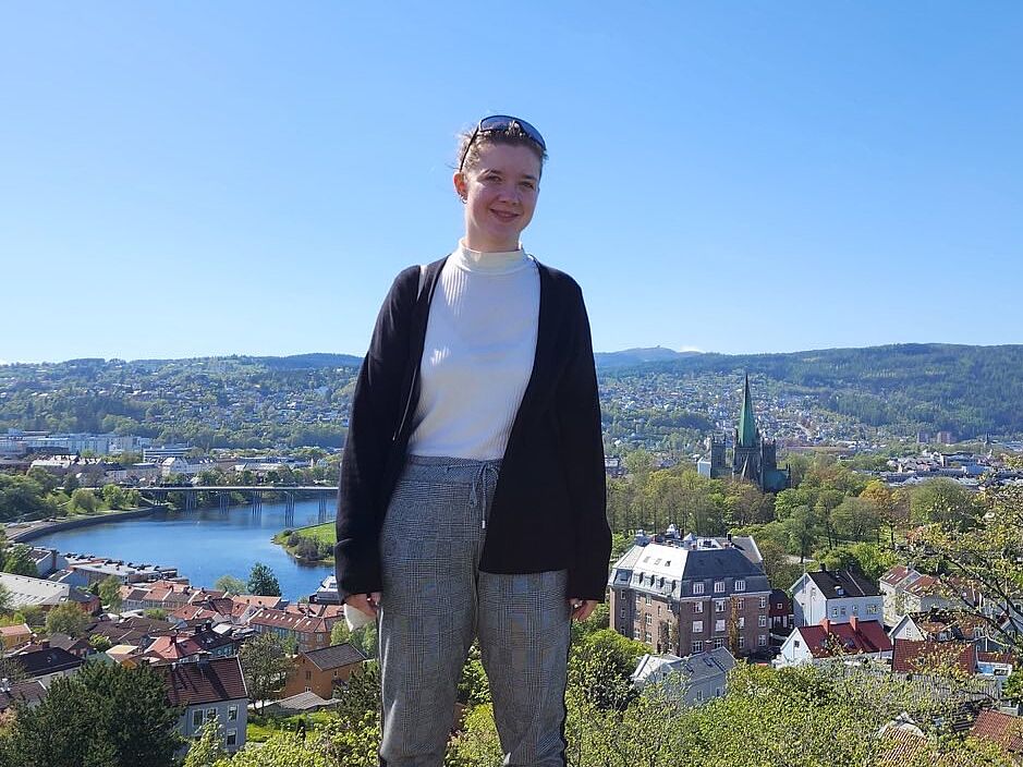Tanja Lösche steht auf einem Aussichtspunkt, im Hintergrund ist eine Stadt und Berglandschaft zu sehen.