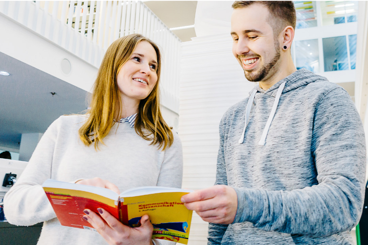 Zwei Studierende in der Bibliothek schauen sich ein Buch an.