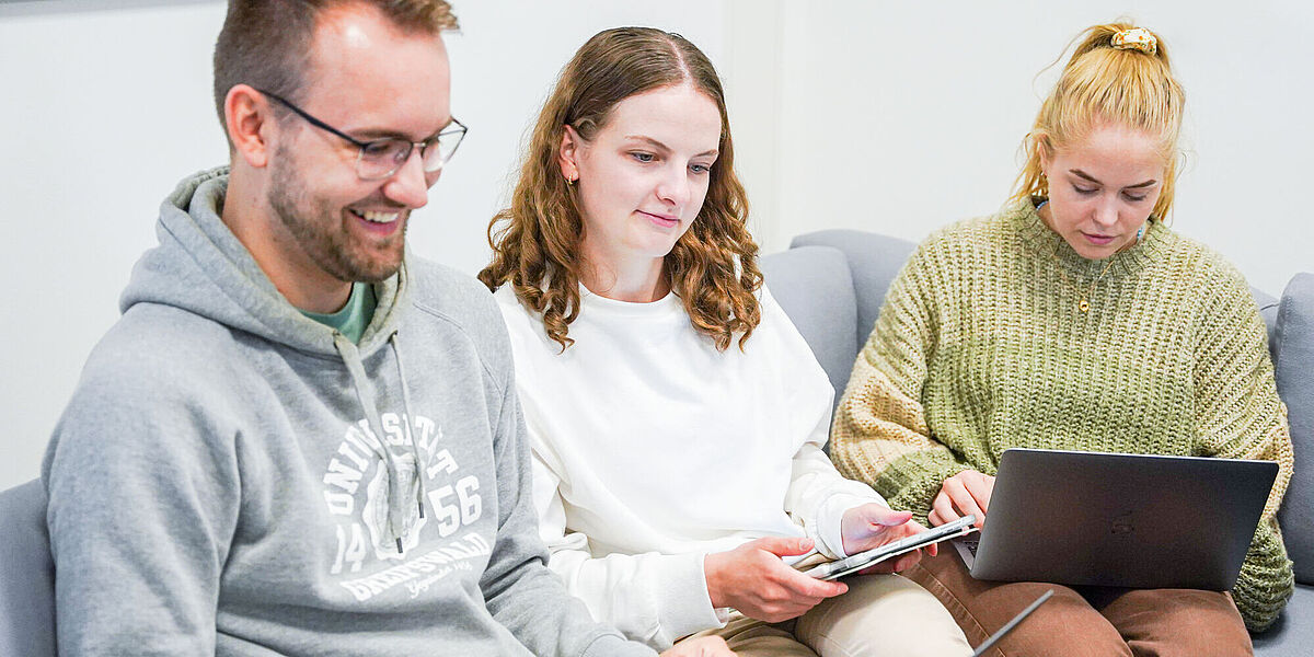 Zwei Studentinnen und ein Student sitzen beisammen und arbeiten an ihren Laptops.